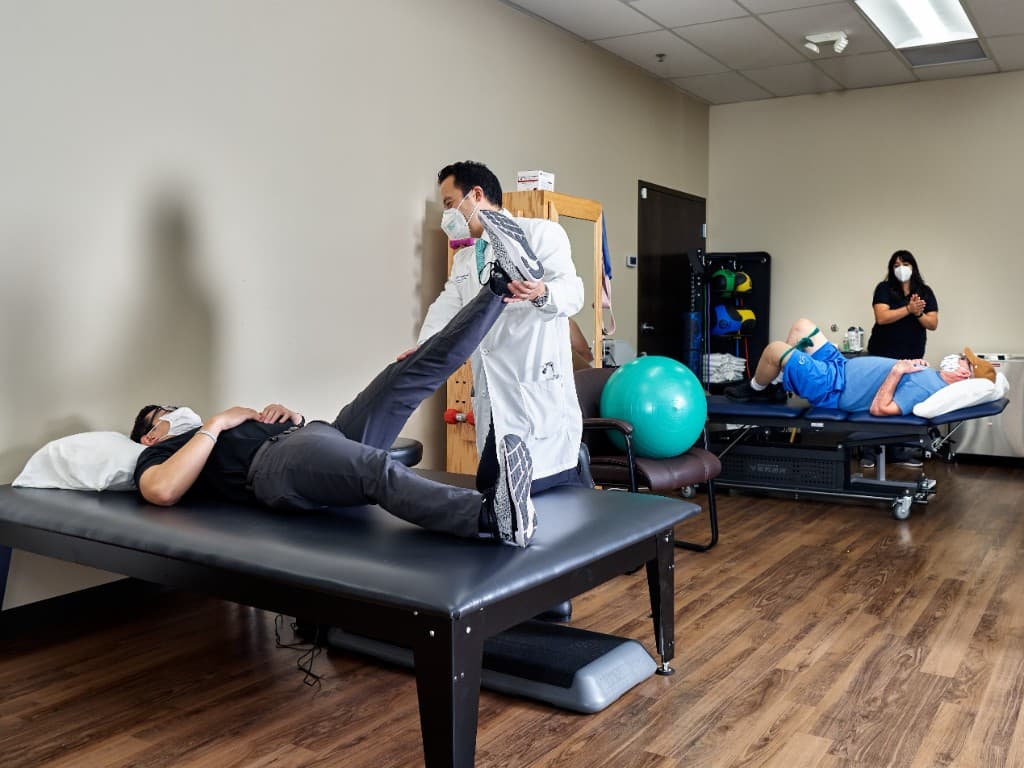 Physician guiding a patient through a supervised leg-raise exercise during a therapy session